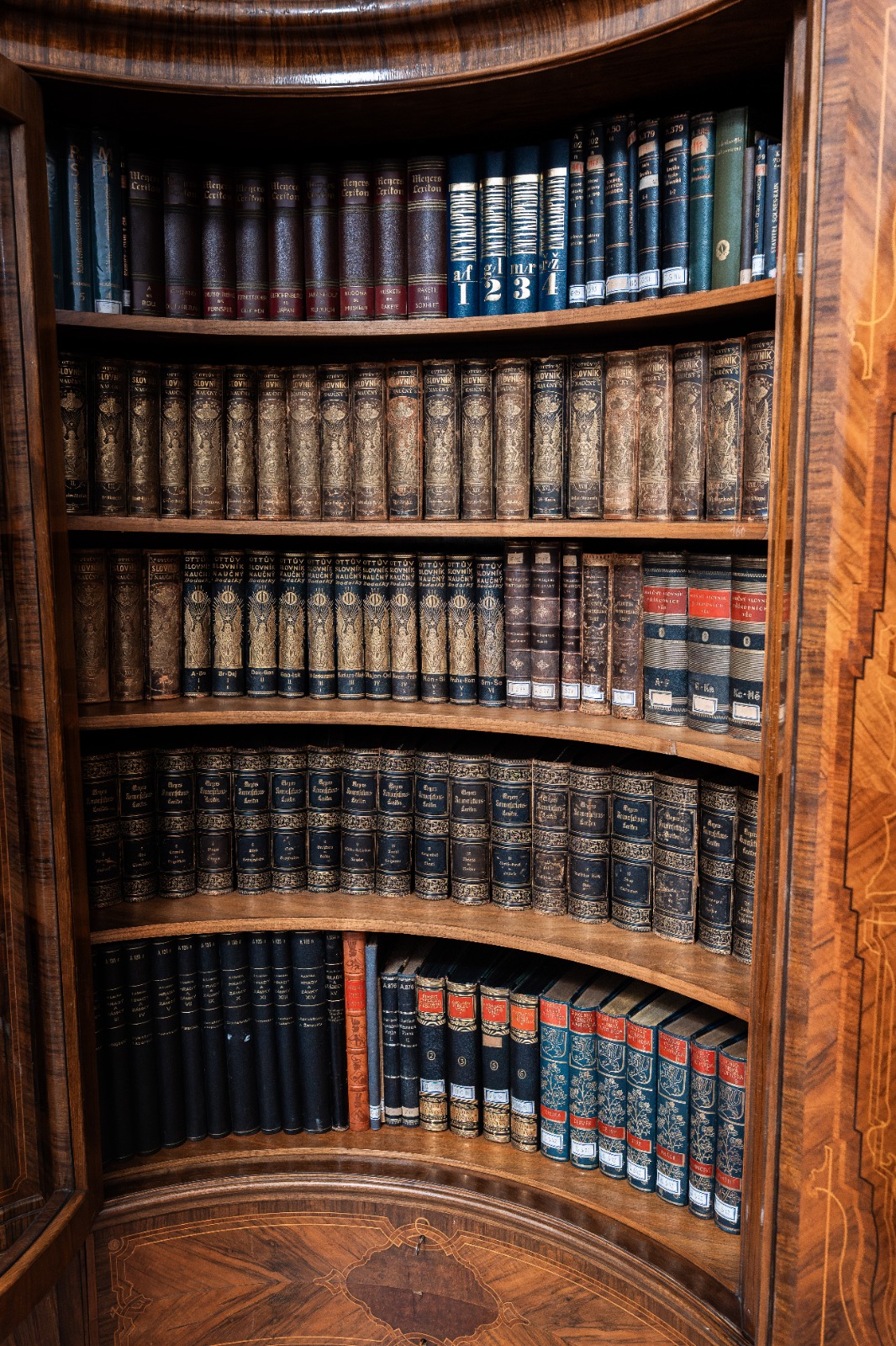 Starobylá dřevěná knihovna s řadami klasických knih, ozdobně vázané svazky na dřevěných policích.