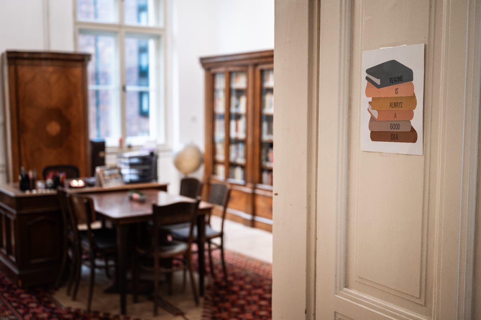 Útulná knihovna s plakátem na dveřích hlásajícím Reading is always a good idea. Dřevěný interiér a knihovny.