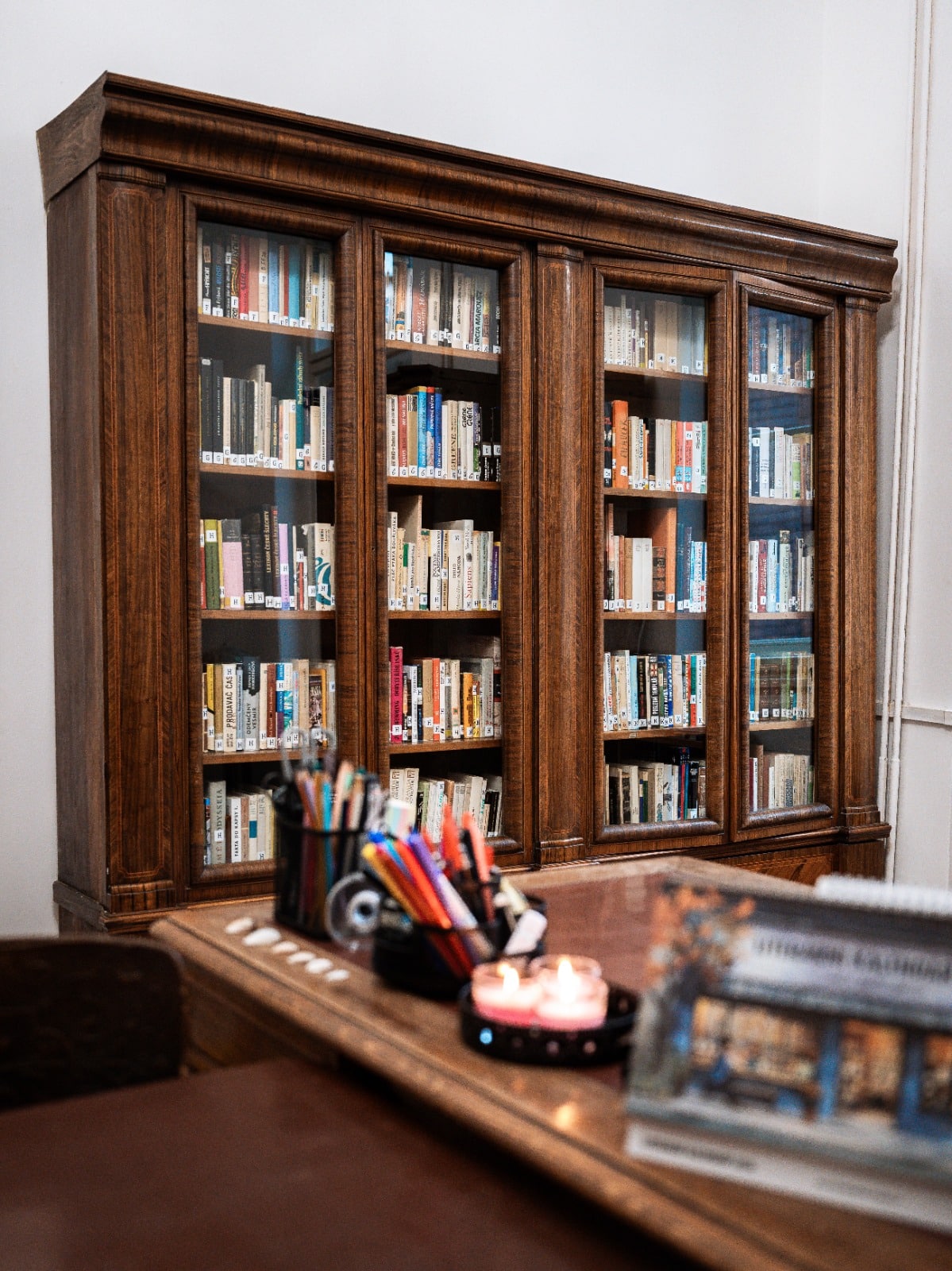 Dřevěná knihovna plná knih s pracovní deskou plnou psacích potřeb a zapálenými svíčkami pro útulné prostředí.