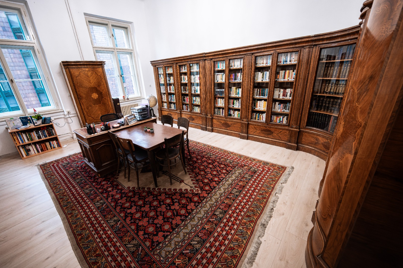 Rustikální knihovna s dřevěným nábytkem, kobercem a zaplněnými policemi pro klidné studium nebo čtení.