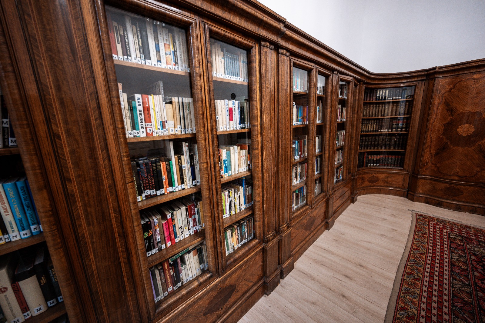 Dřevěná knihovna plná knih s prosklenými dveřmi v elegantním interiéru, ideální pro milovníky literatury.