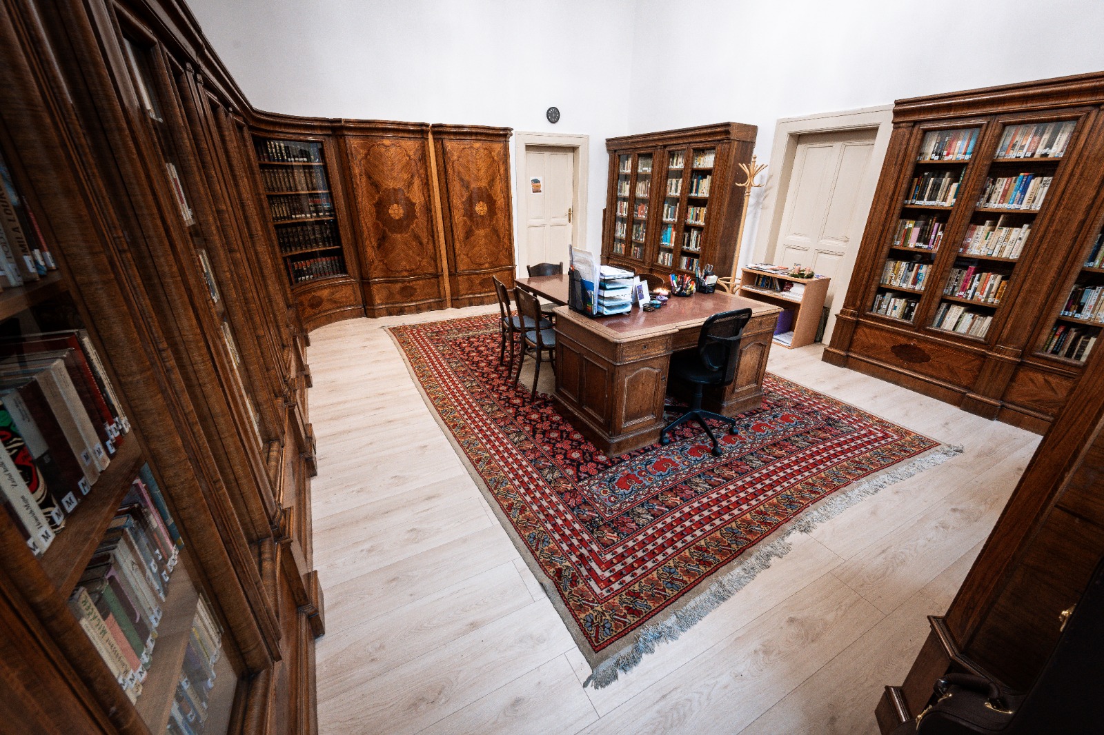 Stará knihovna s dřevěným nábytkem, koberce a regály plné knih, nabízí útulný prostor pro čtení a studium.