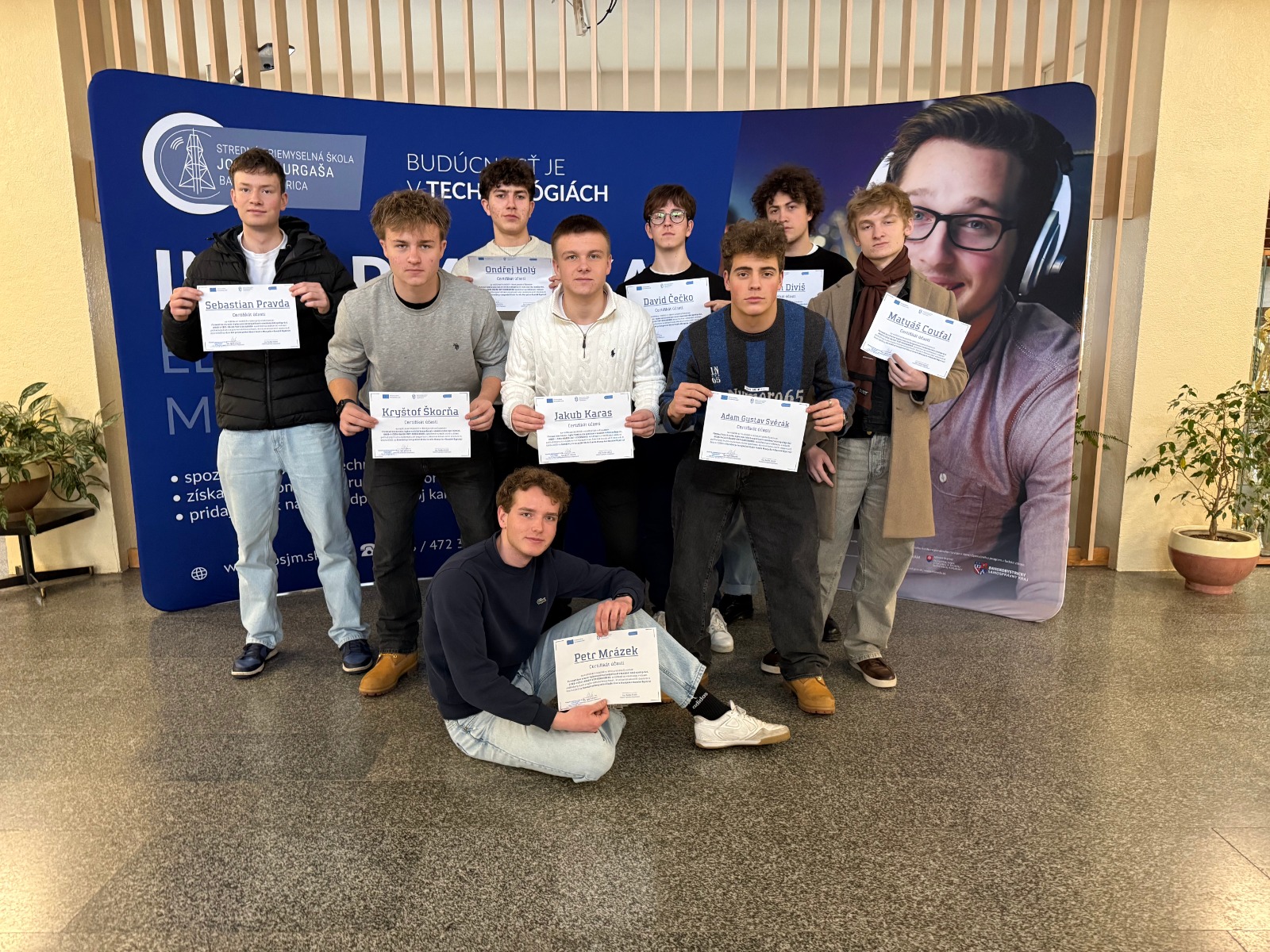 Studenti držící diplomy před nápisem Budoucnost je v technologiích na střední průmyslové škole.